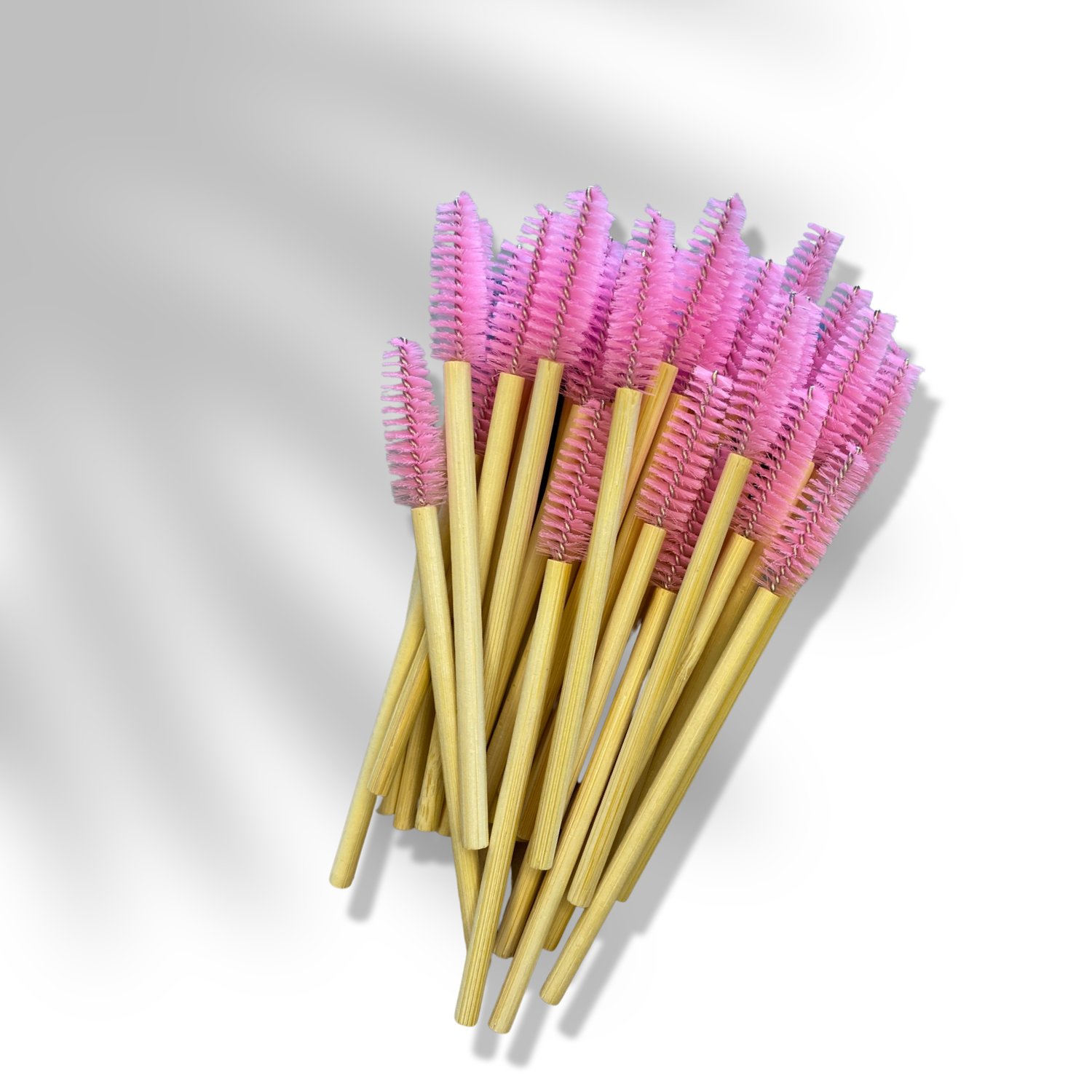 A bunch of brow/lash spoolies with bamboo handles and pink synthetic bristles laying flat.